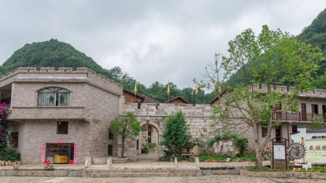 $vo['fname']|default='贵州安顺阿歪寨村是布依族传统村落，位于安顺经开区幺铺镇。该村是三国藤甲兵后裔栖居地，至今保留藤甲编织技艺。村落依山而建，石板路、石墙民居错落分布，布依族刺绣、古法造纸等非遗文化鲜活传承。
图一：古寨门庭
青灰石墙、木构老房围合石板广场，山影浮云里，静泊乡居日常。
图二：乡愁巨石
深灰巨石静卧草坡，“阿歪古寨 留住乡愁”字迹斑驳，野花攀石角，刻下乡土记忆。
图三：守寨武士
黑甲武士雕像擎黄旗立林间，藤甲头盔、长矛静指苍穹，凝住古寨精神脉络。